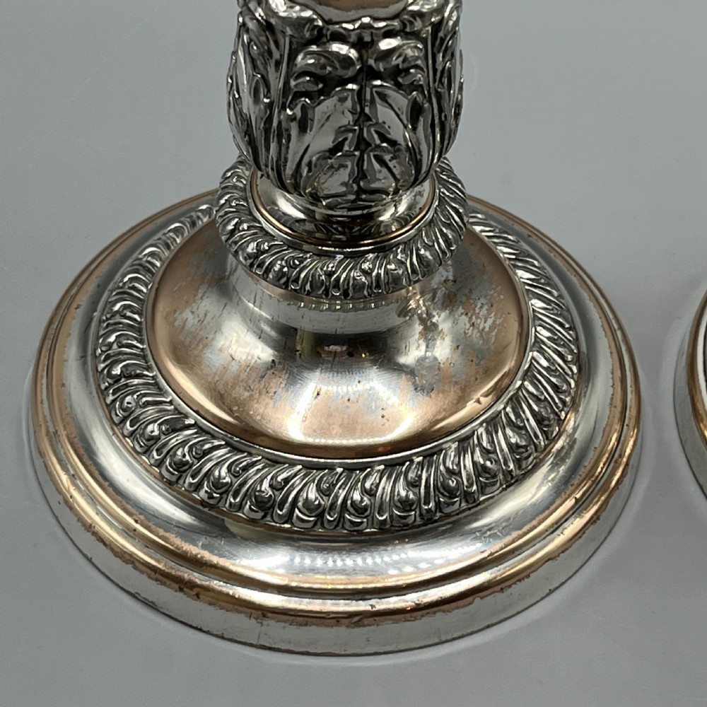 A pair of antique silver-plated candlesticks with gadrooned rims, acanthus leaf details, and exposed copper highlights on round bases. View XI