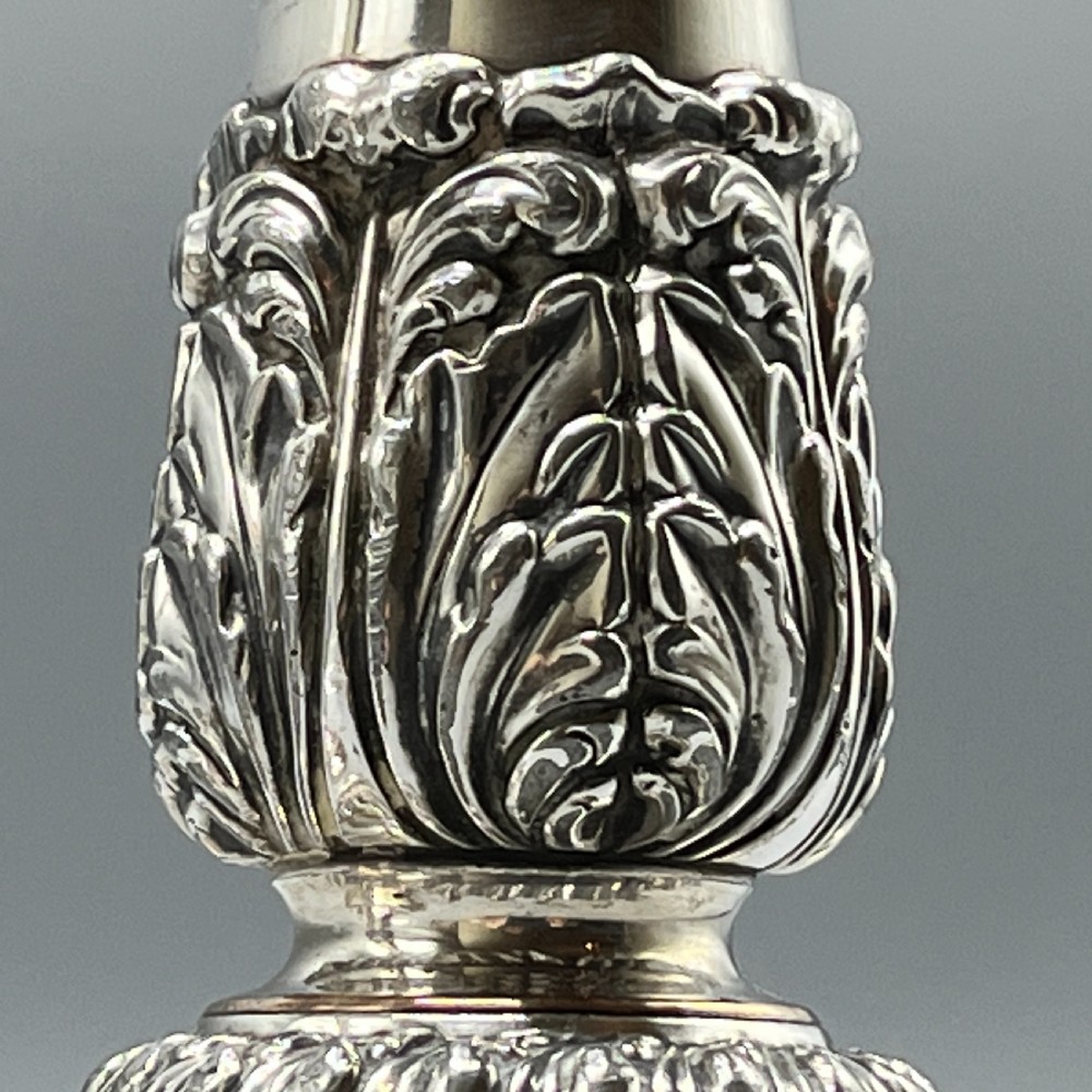 A pair of antique silver-plated candlesticks with gadrooned rims, acanthus leaf details, and exposed copper highlights on round bases. View XII