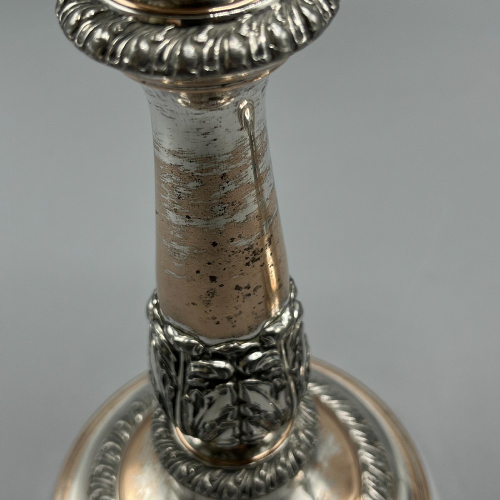 A pair of antique silver-plated candlesticks with gadrooned rims, acanthus leaf details, and exposed copper highlights on round bases. View XIII