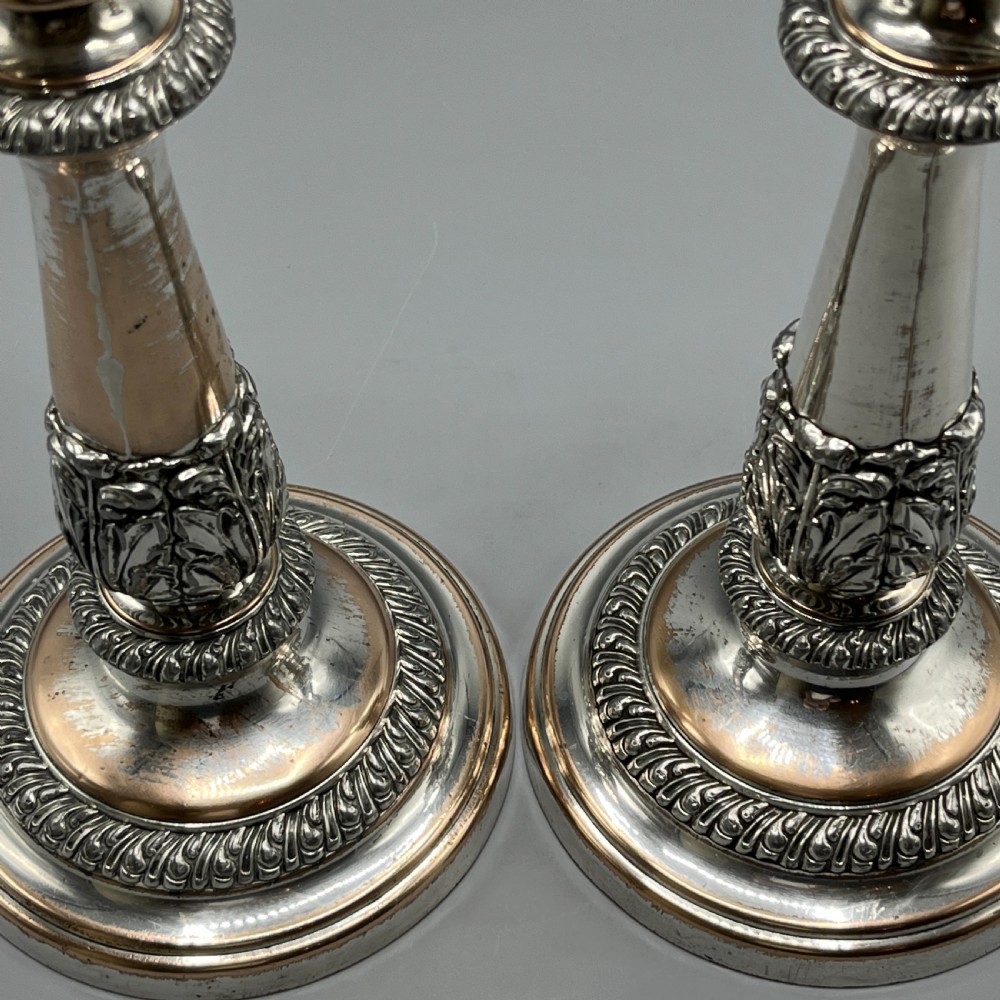 A pair of antique silver-plated candlesticks with gadrooned rims, acanthus leaf details, and exposed copper highlights on round bases. View XIV