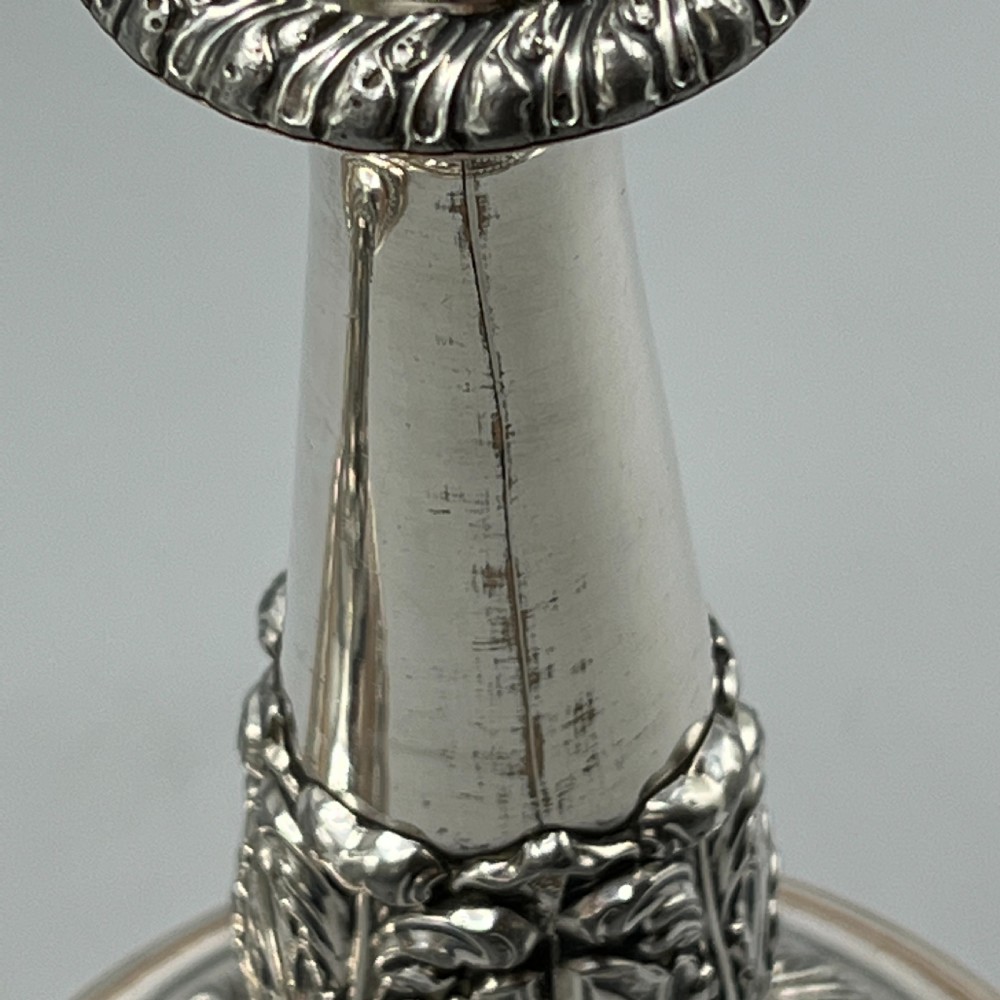 A pair of antique silver-plated candlesticks with gadrooned rims, acanthus leaf details, and exposed copper highlights on round bases. View XV