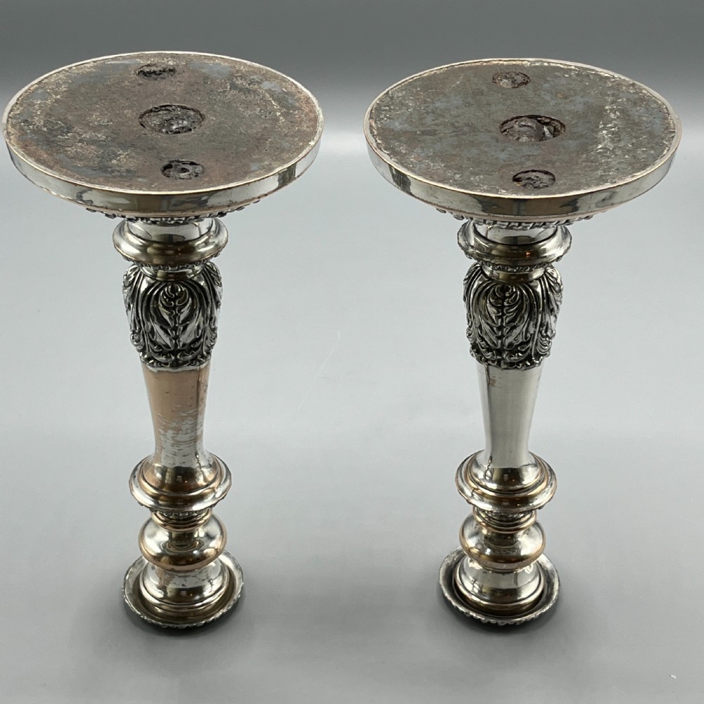 A pair of antique silver-plated candlesticks with gadrooned rims, acanthus leaf details, and exposed copper highlights on round bases. View XVI