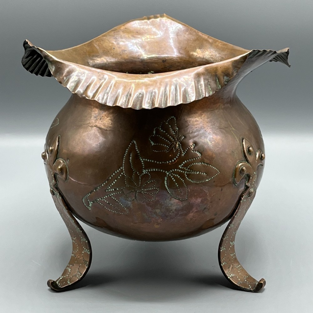 A solid copper Arts and Crafts jardiniere featuring a crimped ruffled rim, dot-punched floral motifs, and riveted splayed legs.