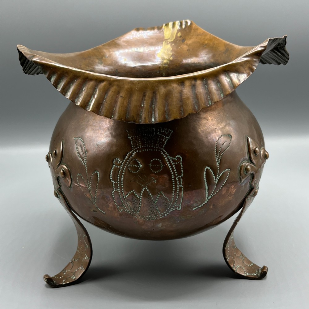 A solid copper Arts and Crafts jardiniere featuring a crimped ruffled rim, dot-punched floral motifs, and riveted splayed legs. View II