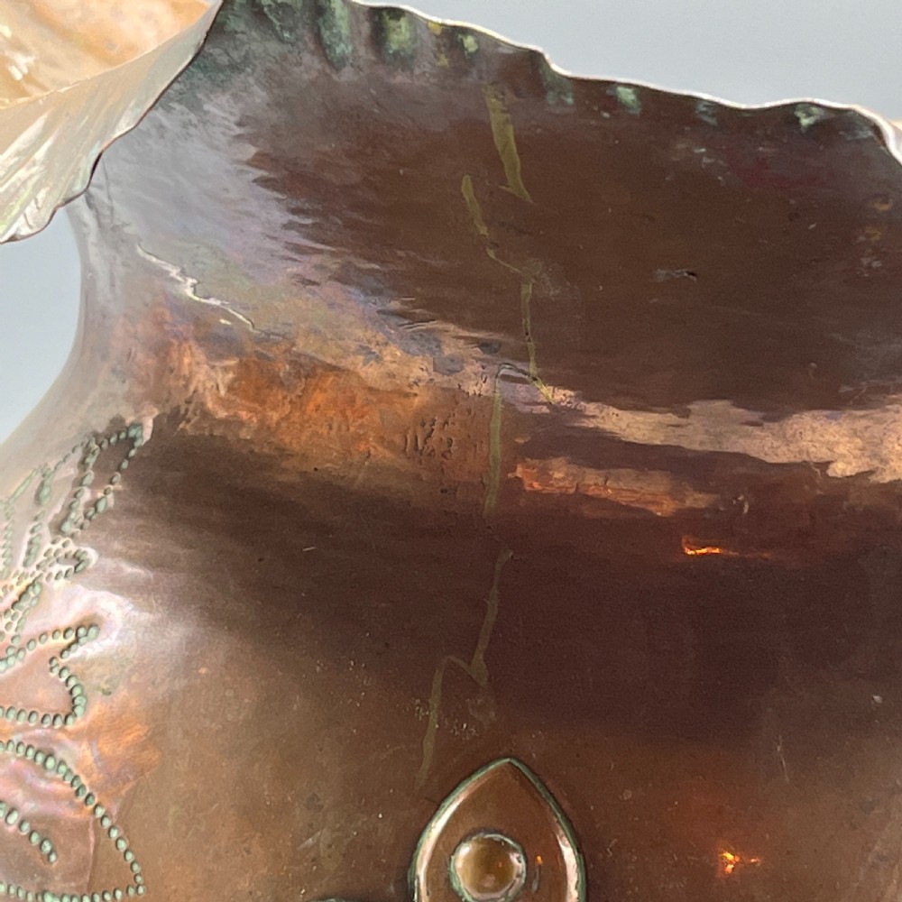 A solid copper Arts and Crafts jardiniere featuring a crimped ruffled rim, dot-punched floral motifs, and riveted splayed legs. View XXII
