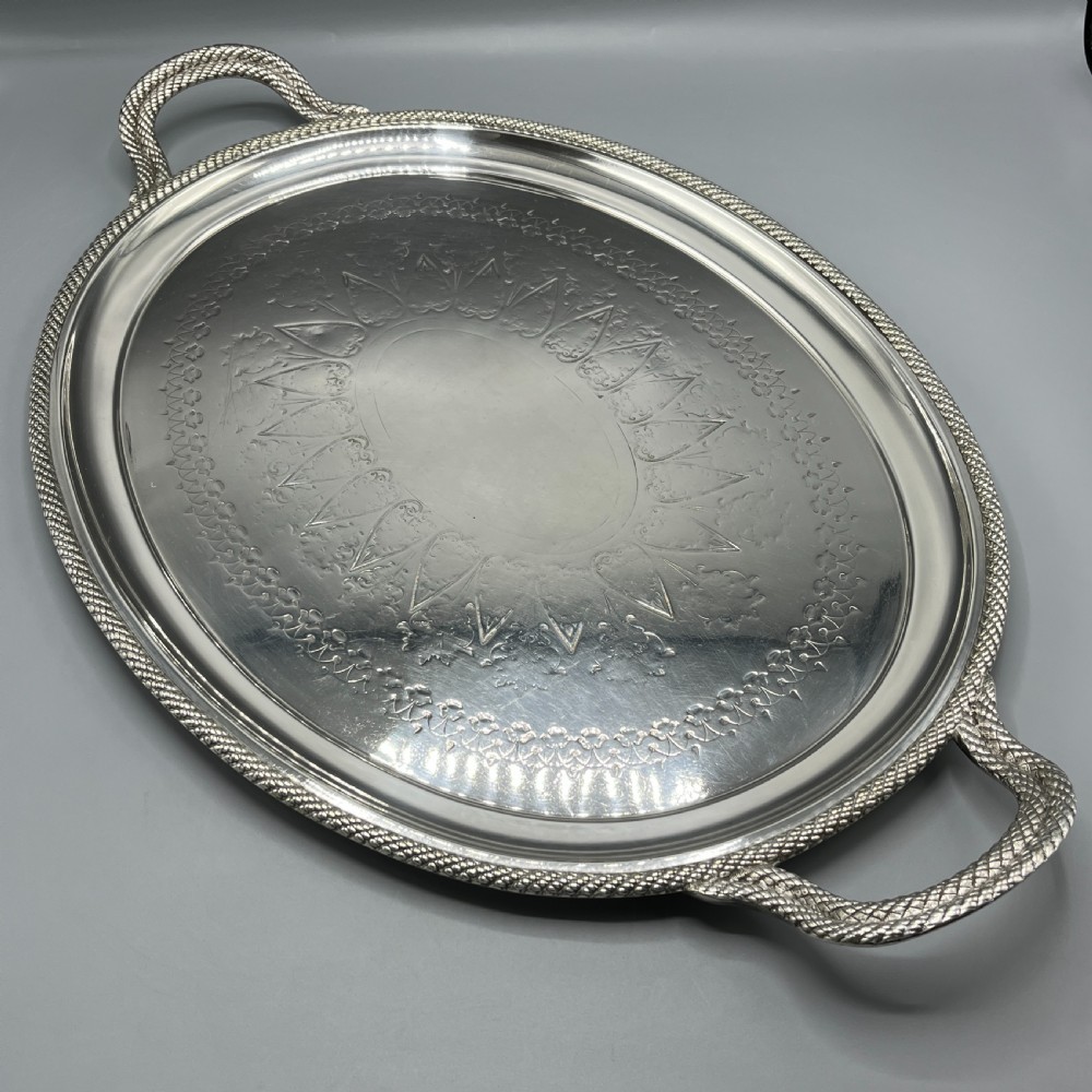 A large Victorian oval silver-plated serving tray featuring twin carrying handles, a textured rope border, and elaborate floral central engraving.