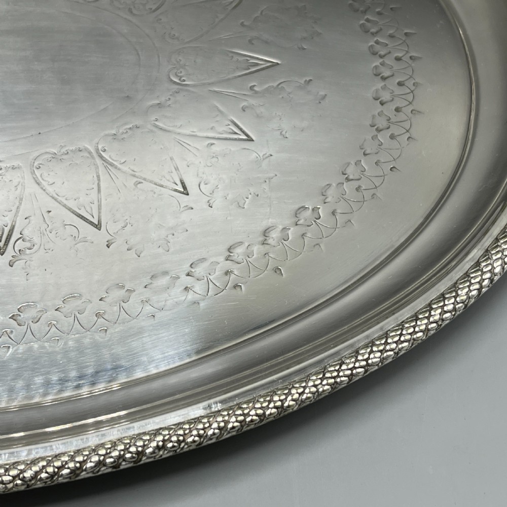 A large Victorian oval silver-plated serving tray featuring twin carrying handles, a textured rope border, and elaborate floral central engraving. View XII
