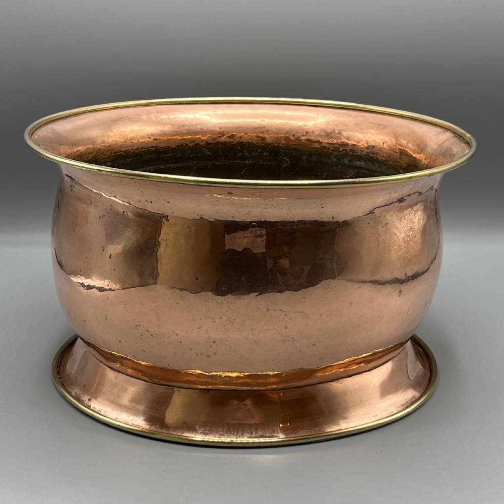 A large polished oval copper jardiniere with a flared rim edged in brass and a fitted flared brass base.