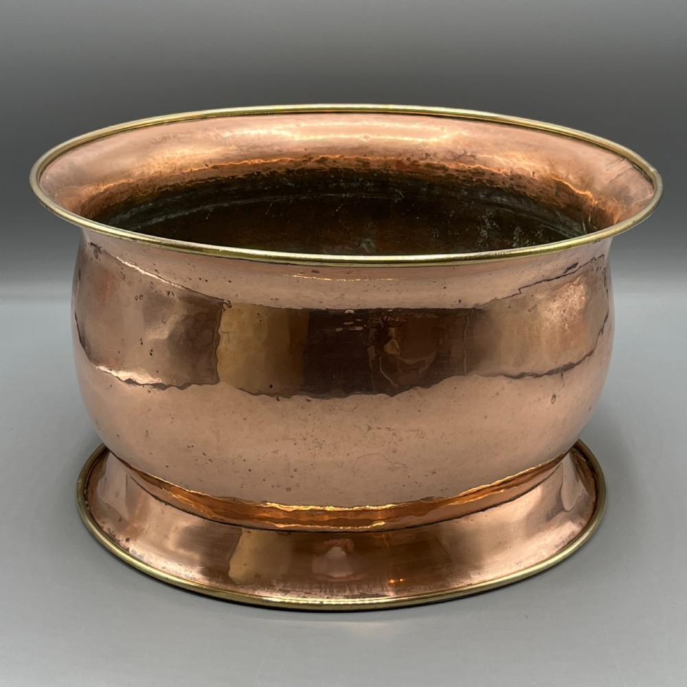 A large polished oval copper jardiniere with a flared rim edged in brass and a fitted flared brass base. View II