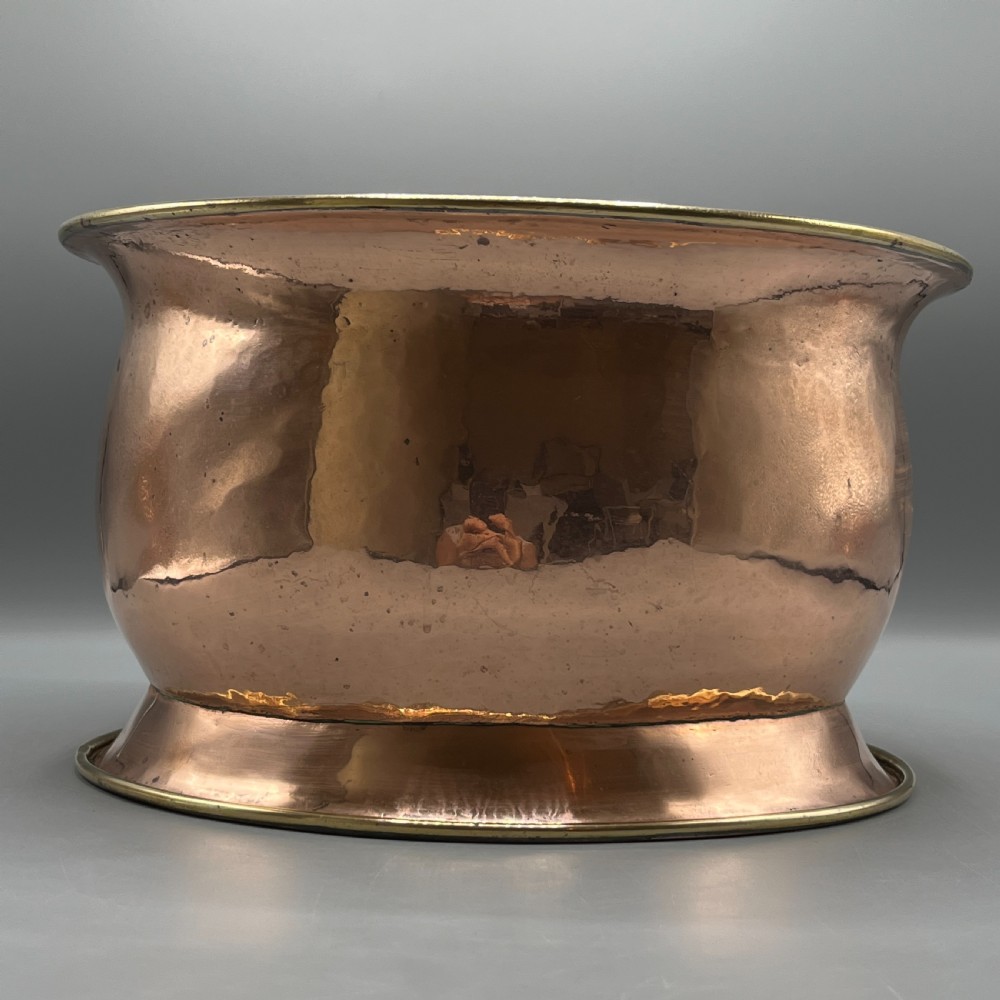 A large polished oval copper jardiniere with a flared rim edged in brass and a fitted flared brass base. View III