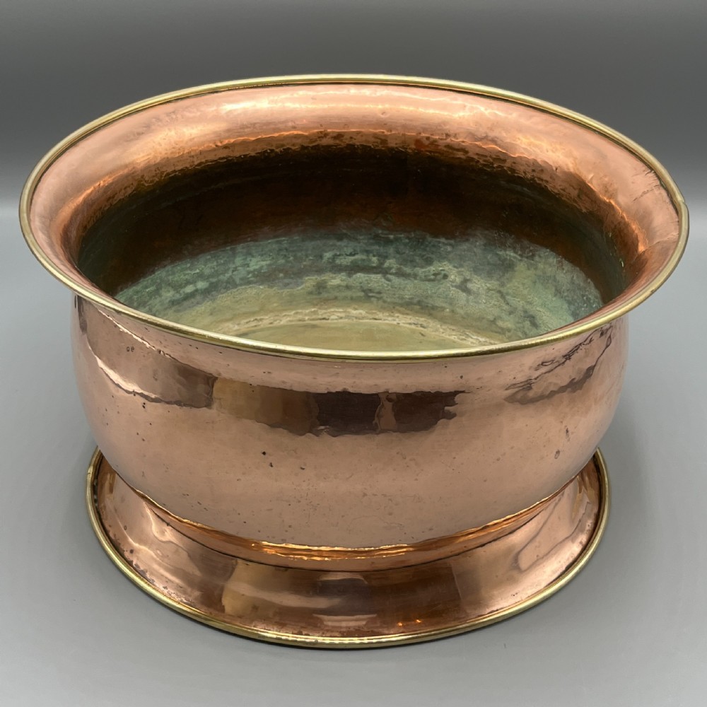 A large polished oval copper jardiniere with a flared rim edged in brass and a fitted flared brass base. View IV