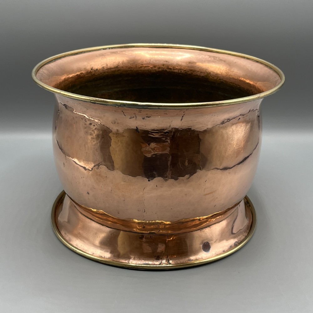 A large polished oval copper jardiniere with a flared rim edged in brass and a fitted flared brass base. View VI