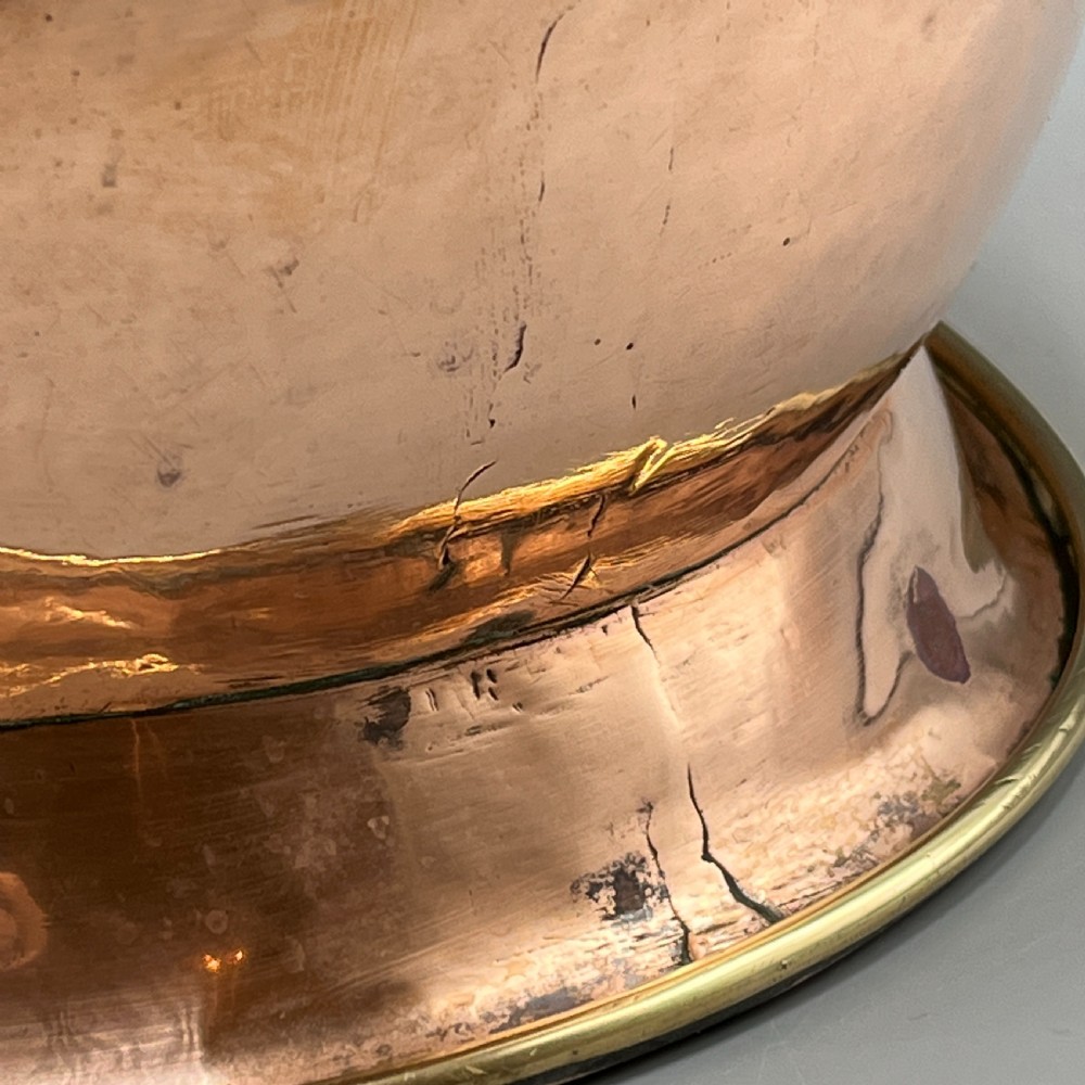 A large polished oval copper jardiniere with a flared rim edged in brass and a fitted flared brass base. View X