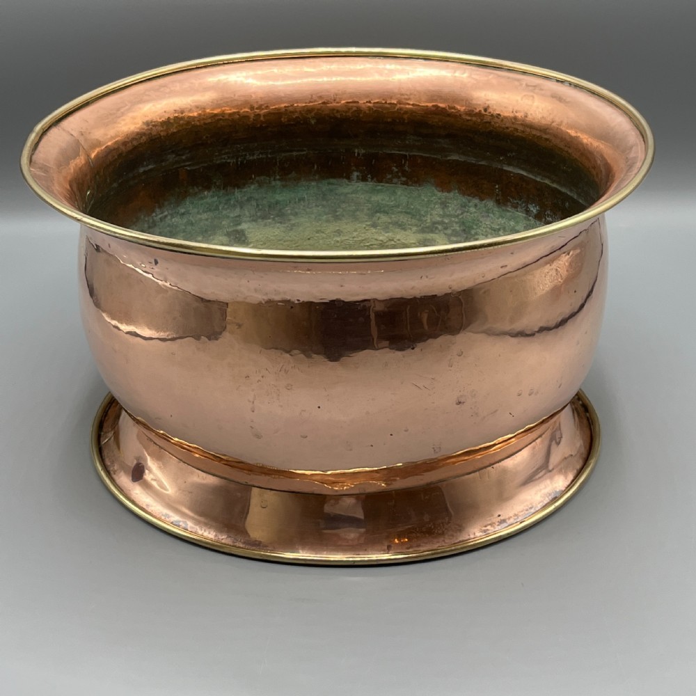 A large polished oval copper jardiniere with a flared rim edged in brass and a fitted flared brass base. View XI