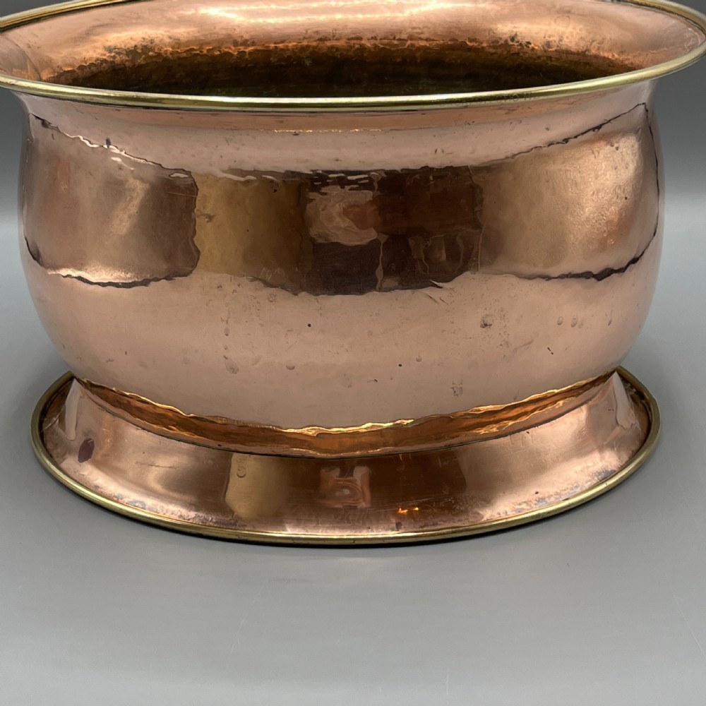 A large polished oval copper jardiniere with a flared rim edged in brass and a fitted flared brass base. View XII