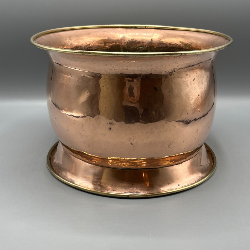 A large polished oval copper jardiniere with a flared rim edged in brass and a fitted flared brass base. View XIV