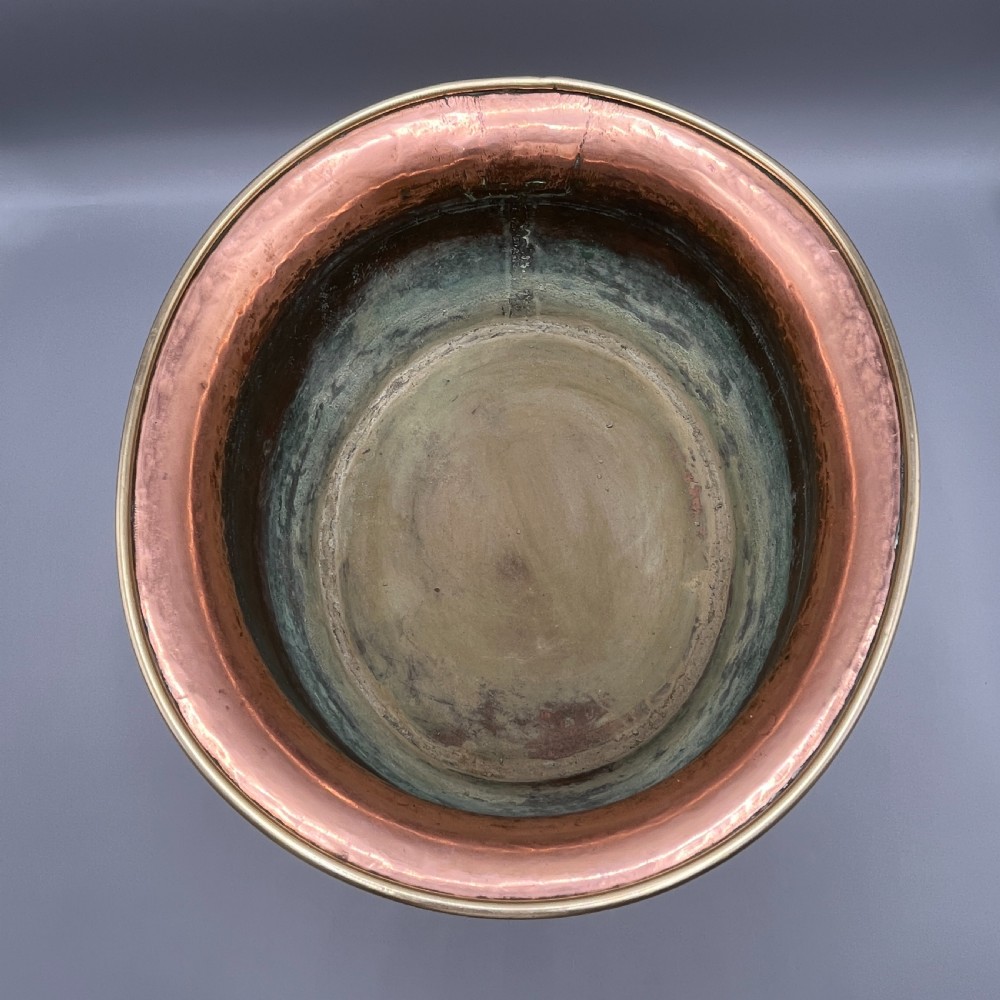 A large polished oval copper jardiniere with a flared rim edged in brass and a fitted flared brass base. View XV