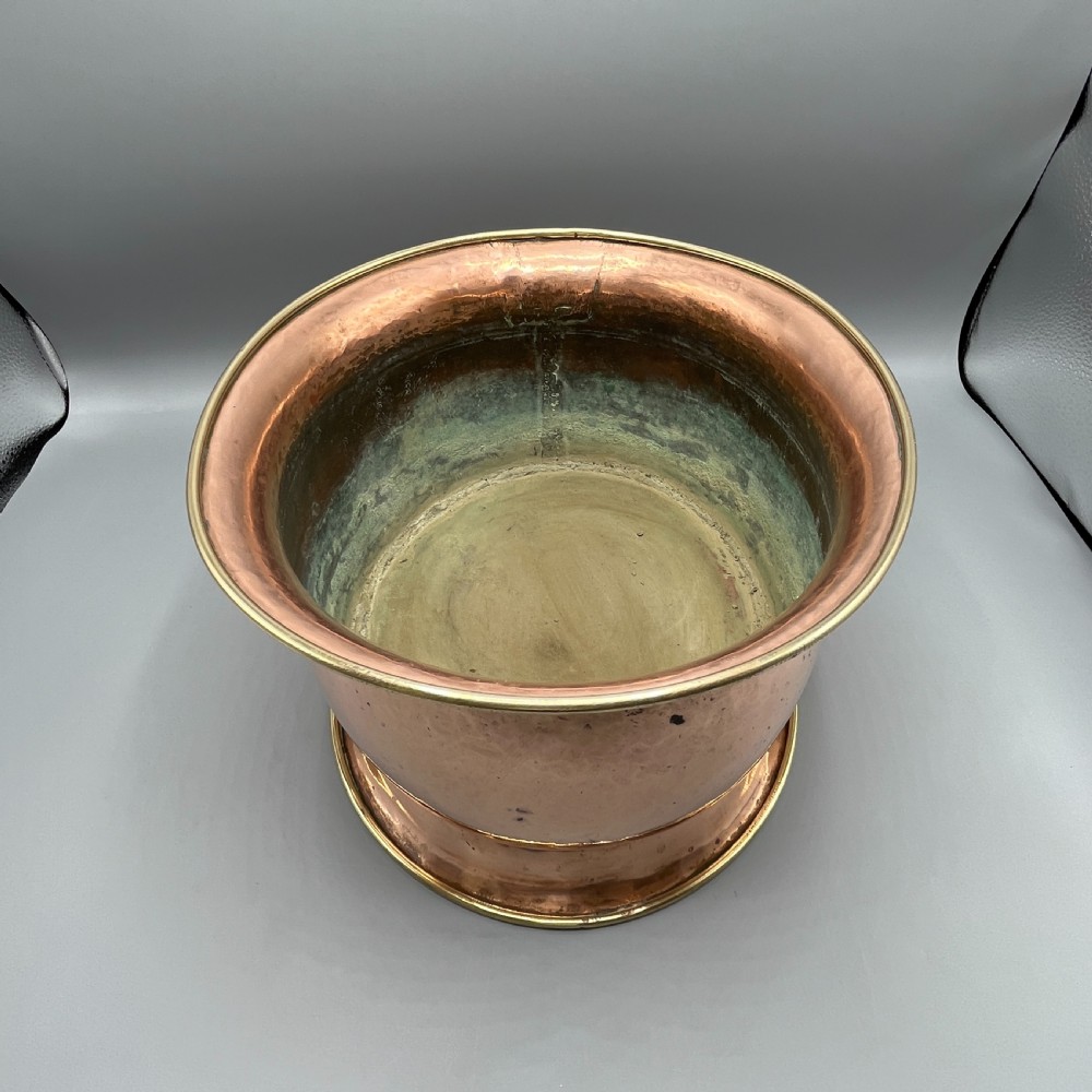 A large polished oval copper jardiniere with a flared rim edged in brass and a fitted flared brass base. View XVI