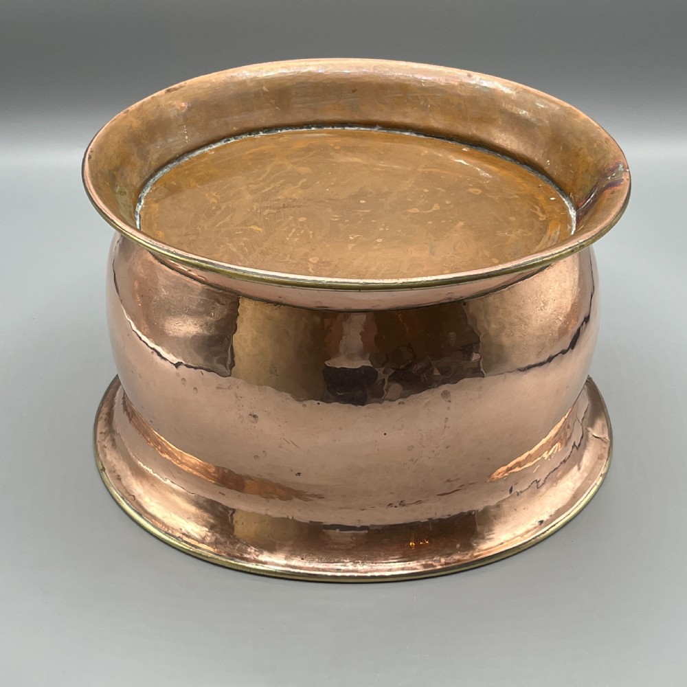 A large polished oval copper jardiniere with a flared rim edged in brass and a fitted flared brass base. View XVIII