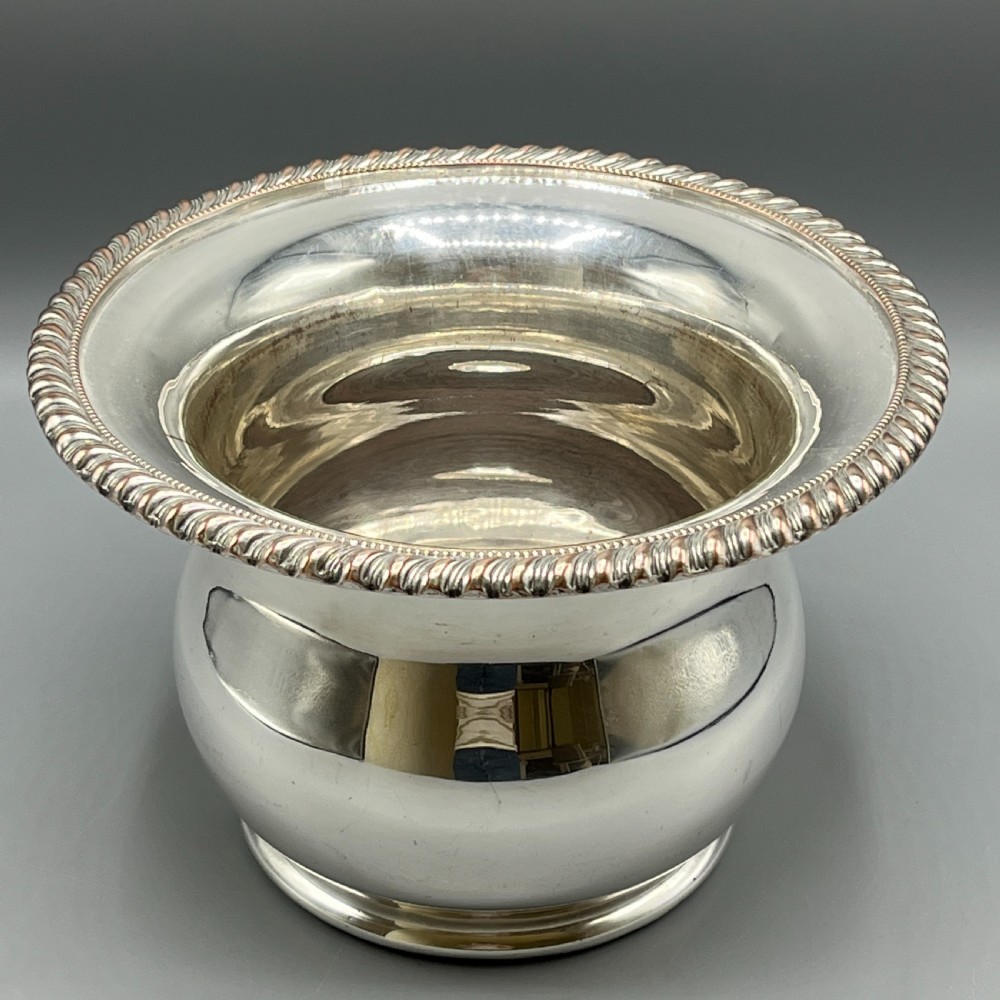 A circular silver-plated wine bottle coaster featuring a rope-twist detailed rim and a flared, polished body.
