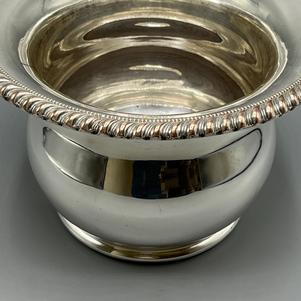 A circular silver-plated wine bottle coaster featuring a rope-twist detailed rim and a flared, polished body. View VII