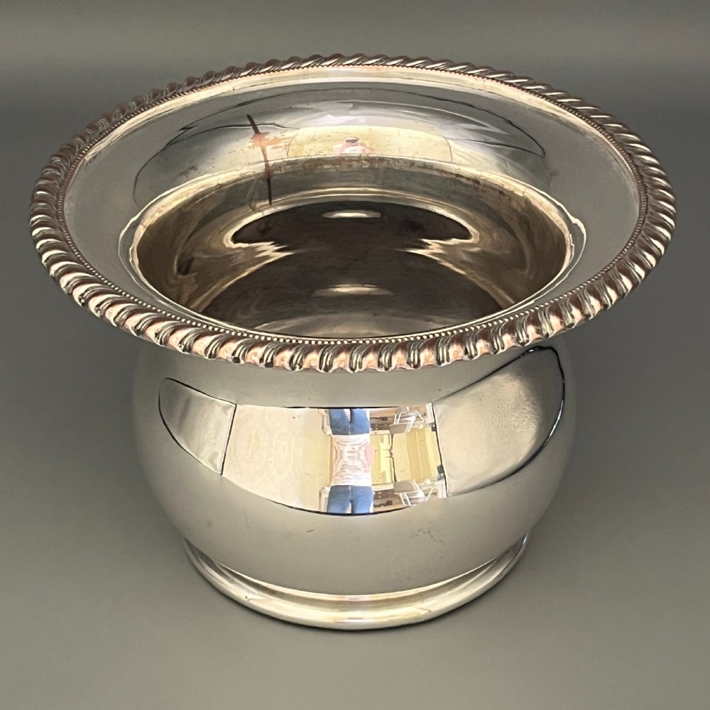 A circular silver-plated wine bottle coaster featuring a rope-twist detailed rim and a flared, polished body. View VIII