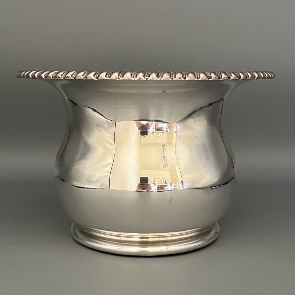 A circular silver-plated wine bottle coaster featuring a rope-twist detailed rim and a flared, polished body. View IX
