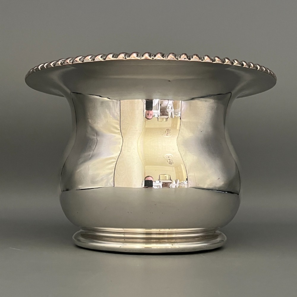 A circular silver-plated wine bottle coaster featuring a rope-twist detailed rim and a flared, polished body. View X