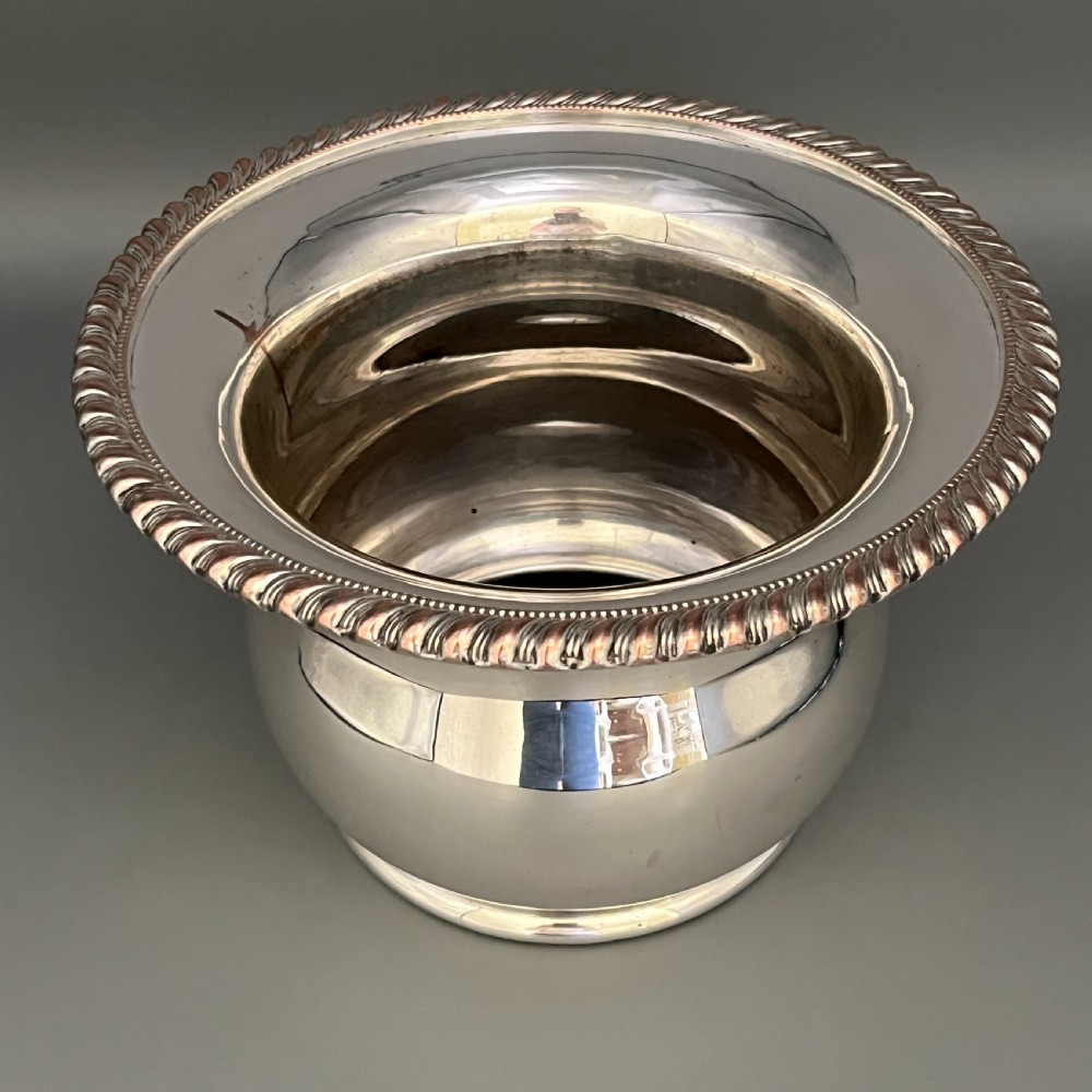 A circular silver-plated wine bottle coaster featuring a rope-twist detailed rim and a flared, polished body. View XV