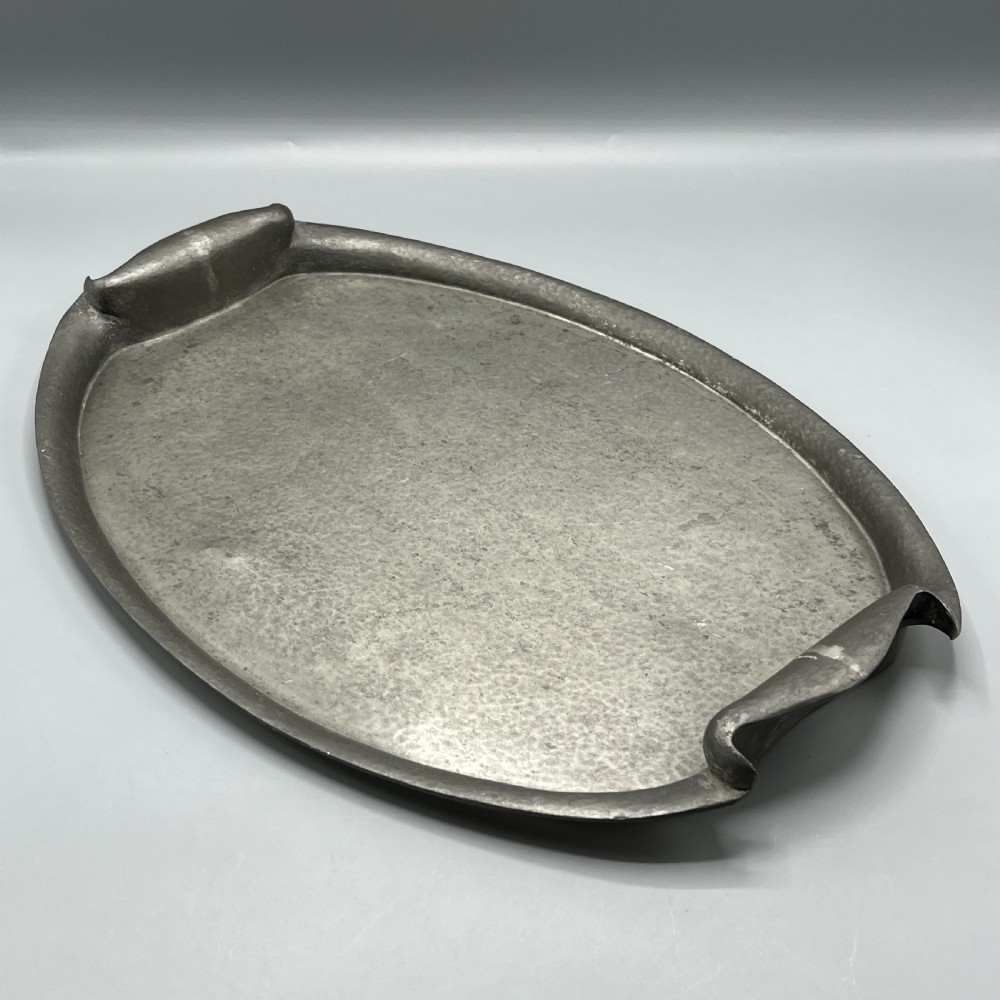 An oval pewter serving tray featuring a hand-hammered surface texture and raised integral handles on opposite ends.