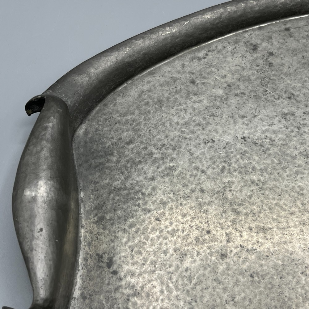 An oval pewter serving tray featuring a hand-hammered surface texture and raised integral handles on opposite ends. View X