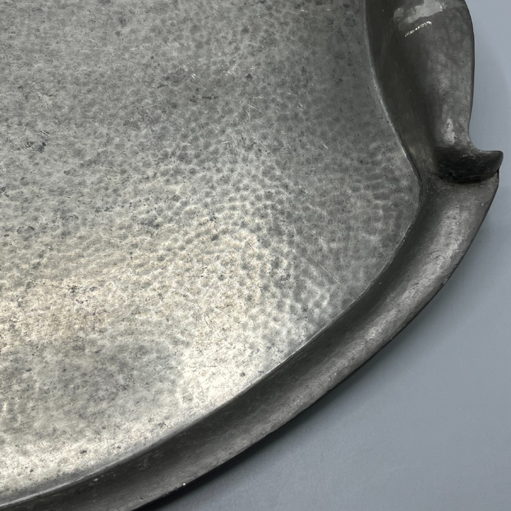 An oval pewter serving tray featuring a hand-hammered surface texture and raised integral handles on opposite ends. View XVII