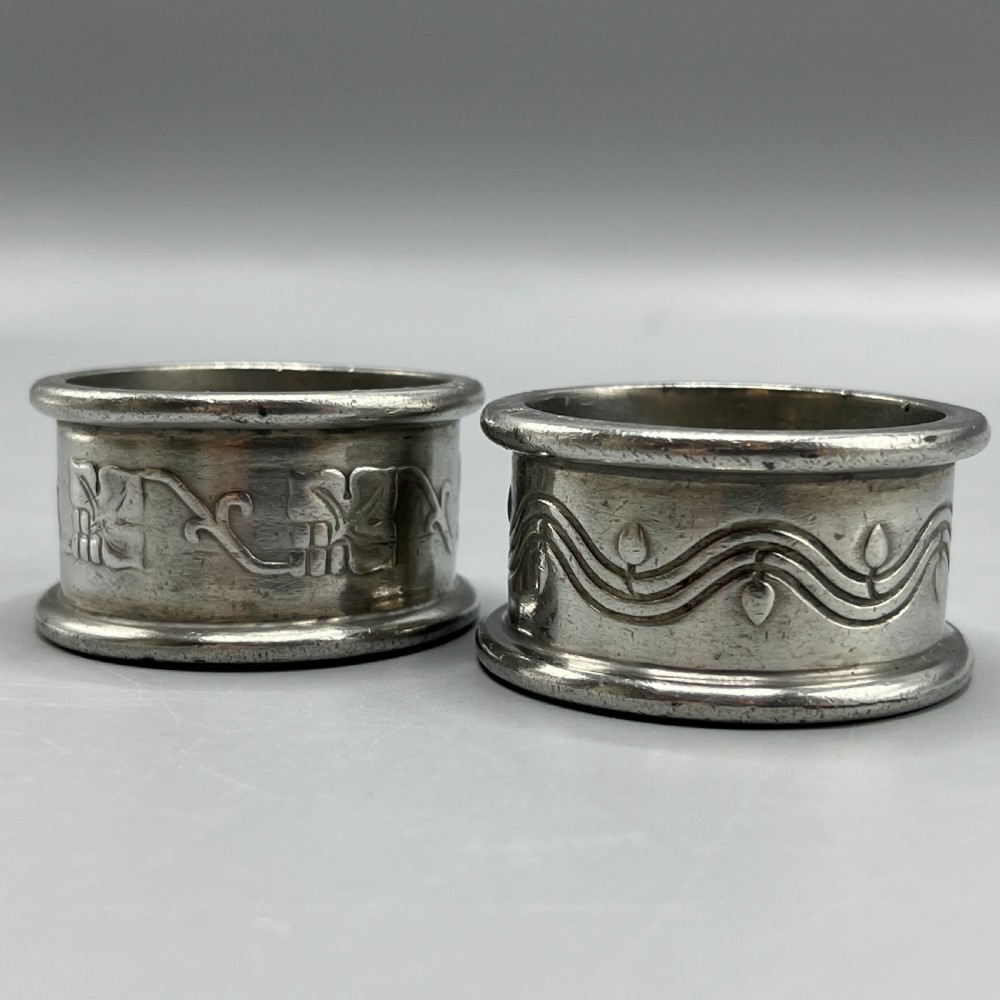 A pair of circular pewter napkin rings decorated with embossed Arts and Crafts stylised floral and tendril motifs.