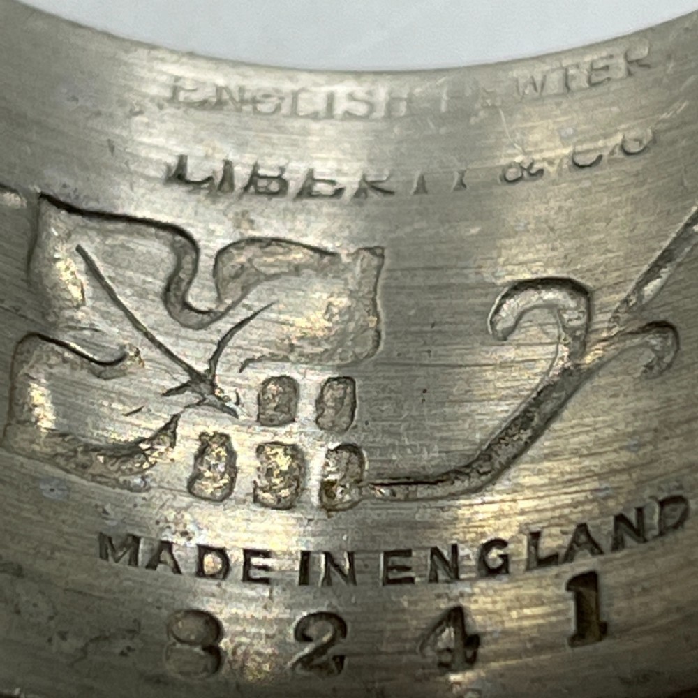 A pair of circular pewter napkin rings decorated with embossed Arts and Crafts stylised floral and tendril motifs. View X