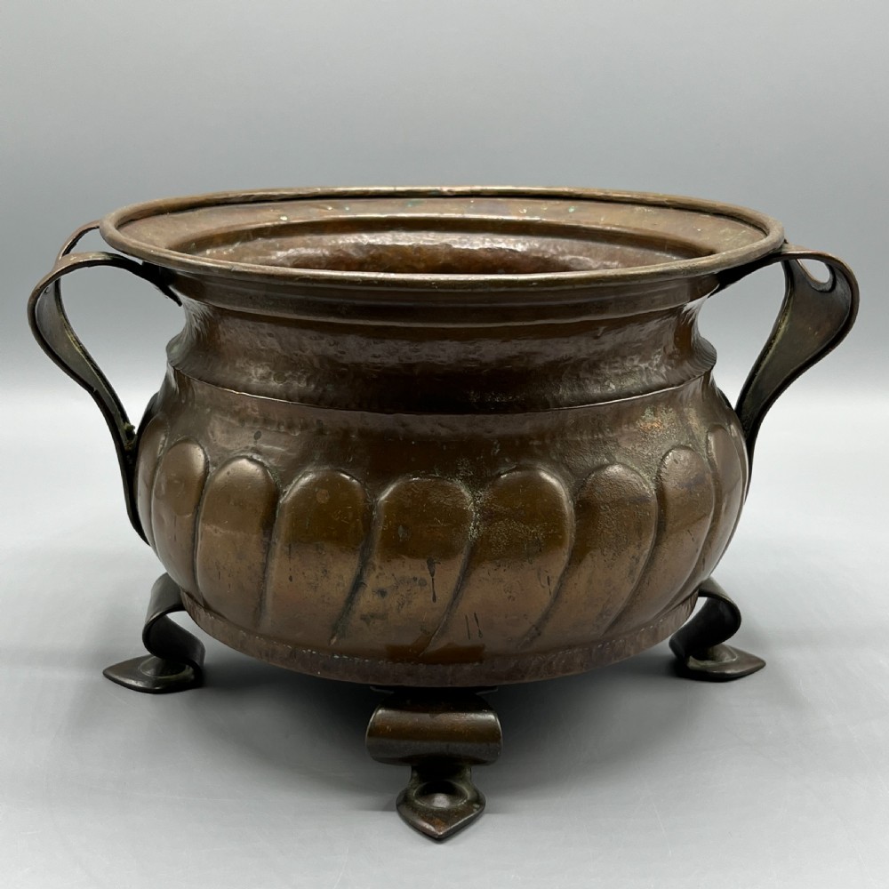 A hand-hammered solid copper Arts and Crafts jardiniere featuring curved side handles, lobed lower body detailing, and four raised feet. View II