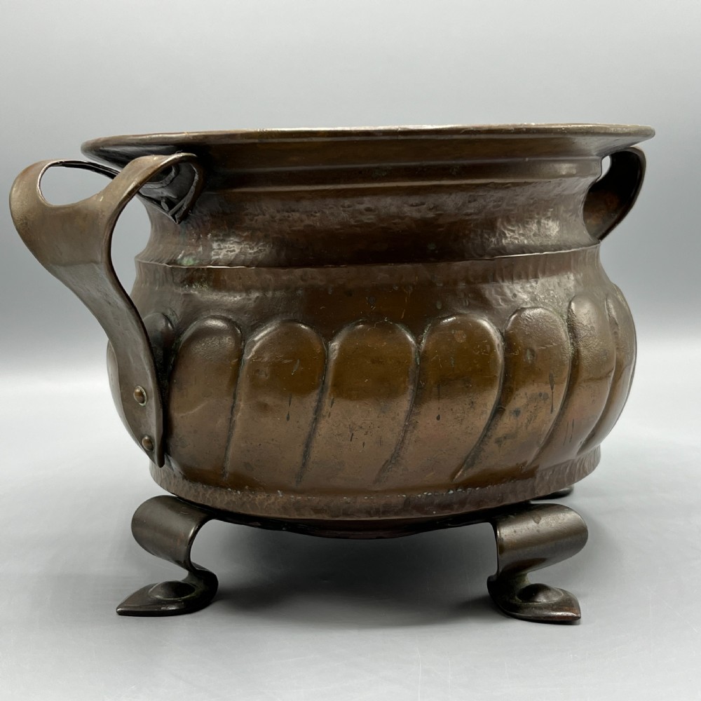 A hand-hammered solid copper Arts and Crafts jardiniere featuring curved side handles, lobed lower body detailing, and four raised feet. View IV