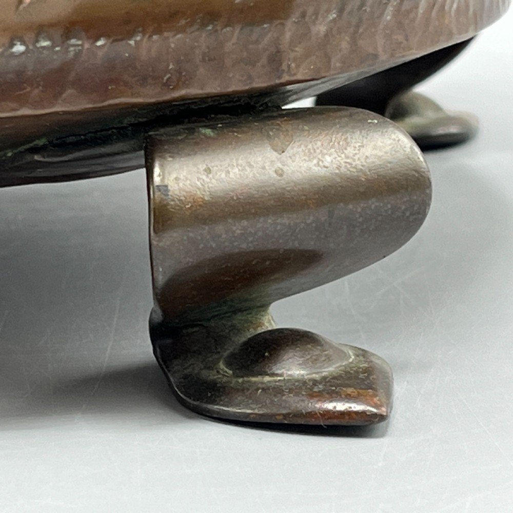 A hand-hammered solid copper Arts and Crafts jardiniere featuring curved side handles, lobed lower body detailing, and four raised feet. View V