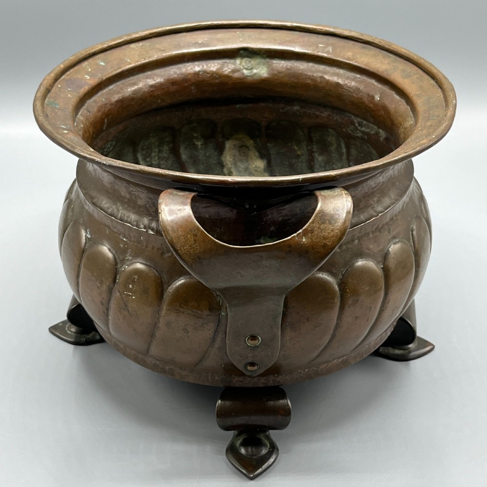 A hand-hammered solid copper Arts and Crafts jardiniere featuring curved side handles, lobed lower body detailing, and four raised feet. View VII