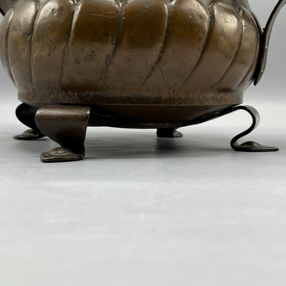 A hand-hammered solid copper Arts and Crafts jardiniere featuring curved side handles, lobed lower body detailing, and four raised feet. View VIII