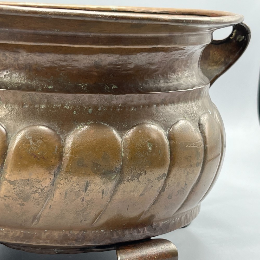 A hand-hammered solid copper Arts and Crafts jardiniere featuring curved side handles, lobed lower body detailing, and four raised feet. View IX