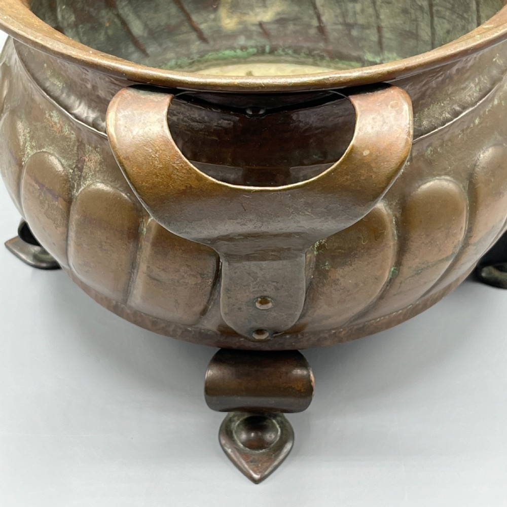 A hand-hammered solid copper Arts and Crafts jardiniere featuring curved side handles, lobed lower body detailing, and four raised feet. View XI