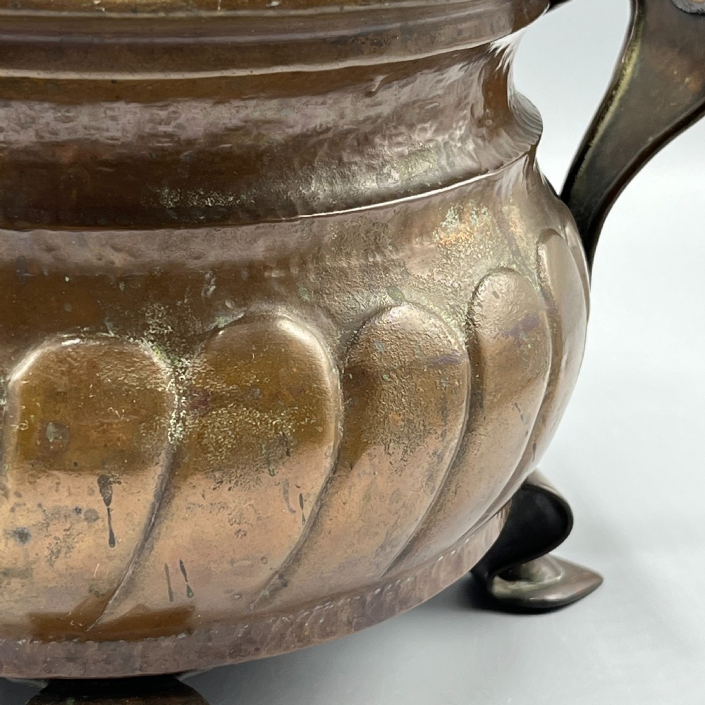 A hand-hammered solid copper Arts and Crafts jardiniere featuring curved side handles, lobed lower body detailing, and four raised feet. View XII