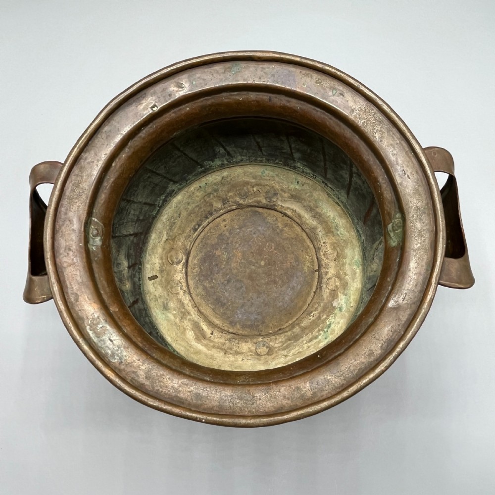 A hand-hammered solid copper Arts and Crafts jardiniere featuring curved side handles, lobed lower body detailing, and four raised feet. View XIV