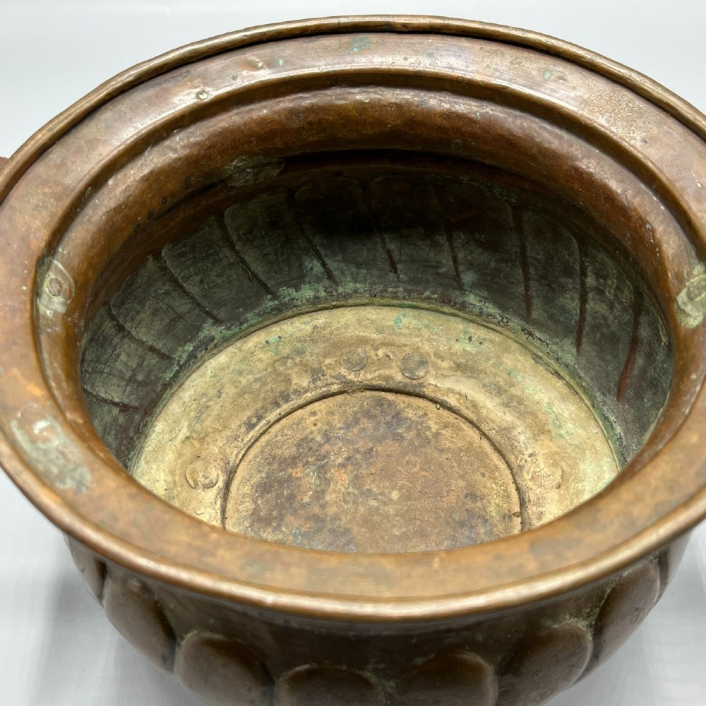 A hand-hammered solid copper Arts and Crafts jardiniere featuring curved side handles, lobed lower body detailing, and four raised feet. View XV