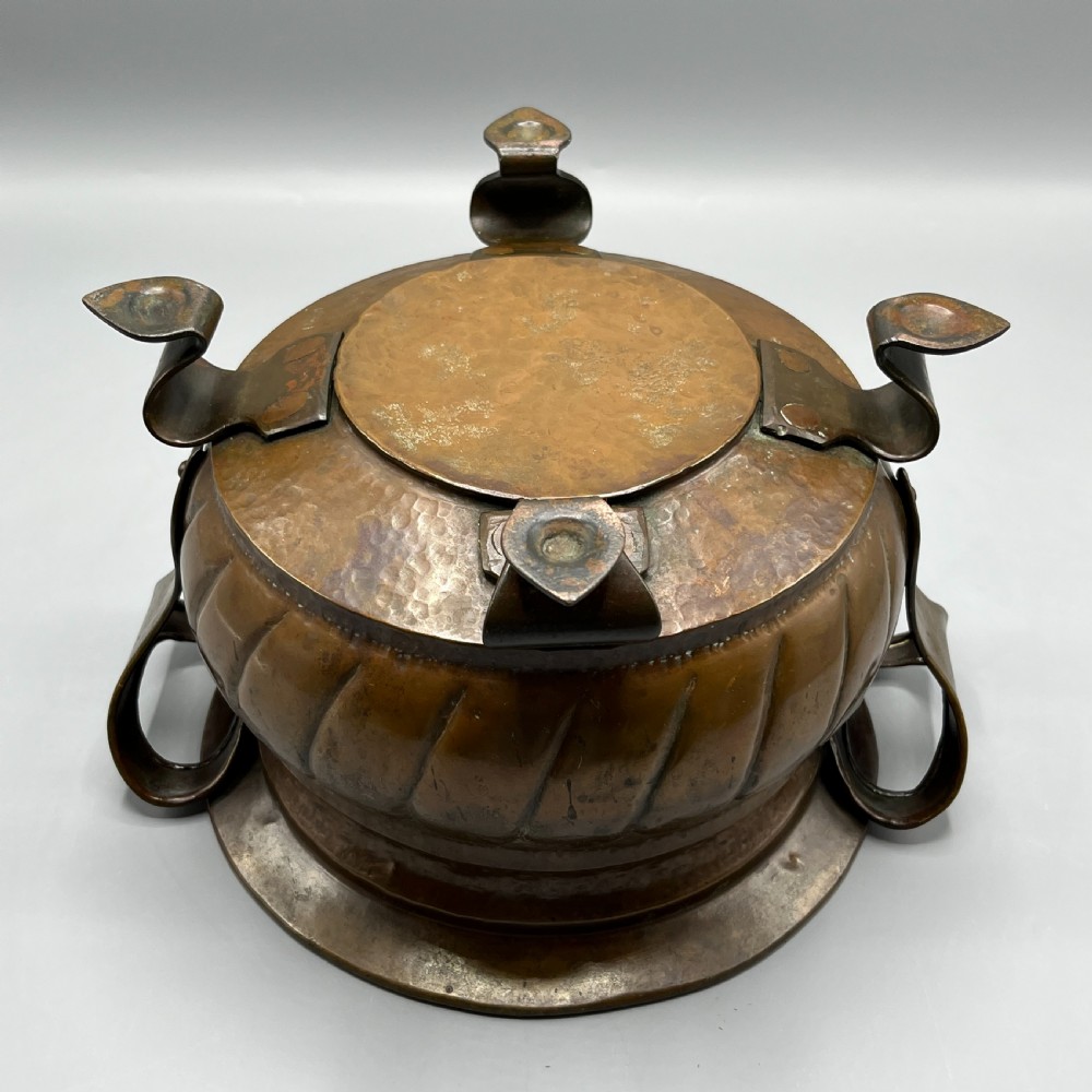 A hand-hammered solid copper Arts and Crafts jardiniere featuring curved side handles, lobed lower body detailing, and four raised feet. View XVI