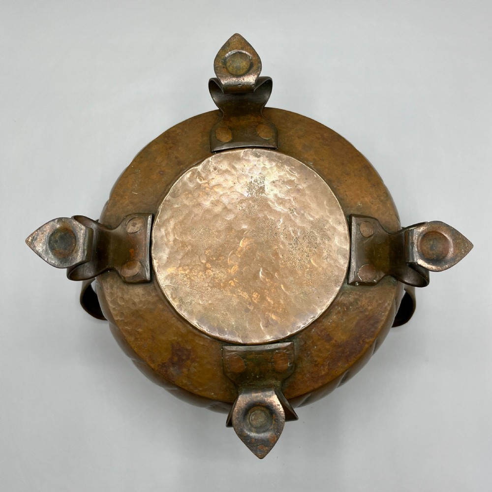 A hand-hammered solid copper Arts and Crafts jardiniere featuring curved side handles, lobed lower body detailing, and four raised feet. View XVII