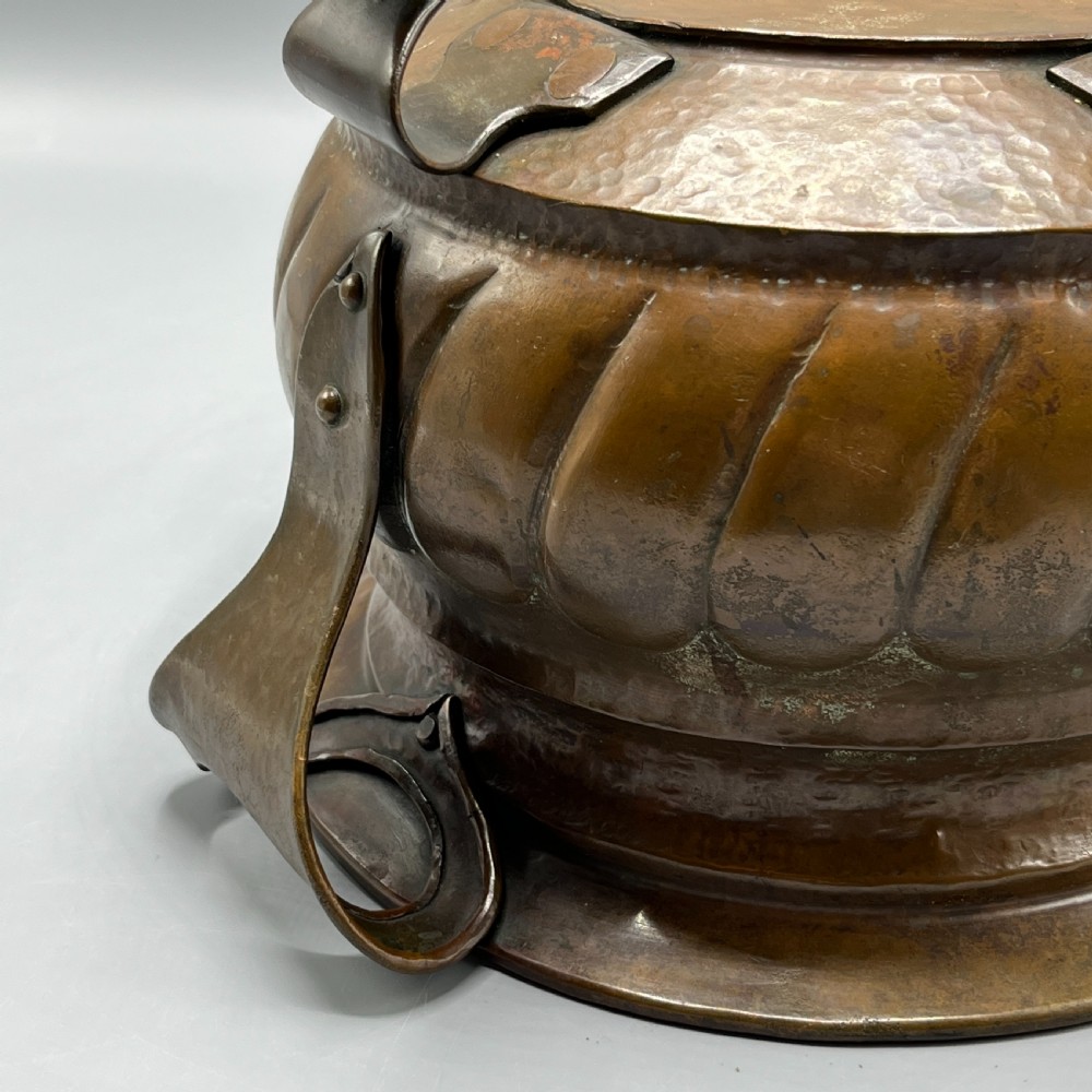 A hand-hammered solid copper Arts and Crafts jardiniere featuring curved side handles, lobed lower body detailing, and four raised feet. View XVIII