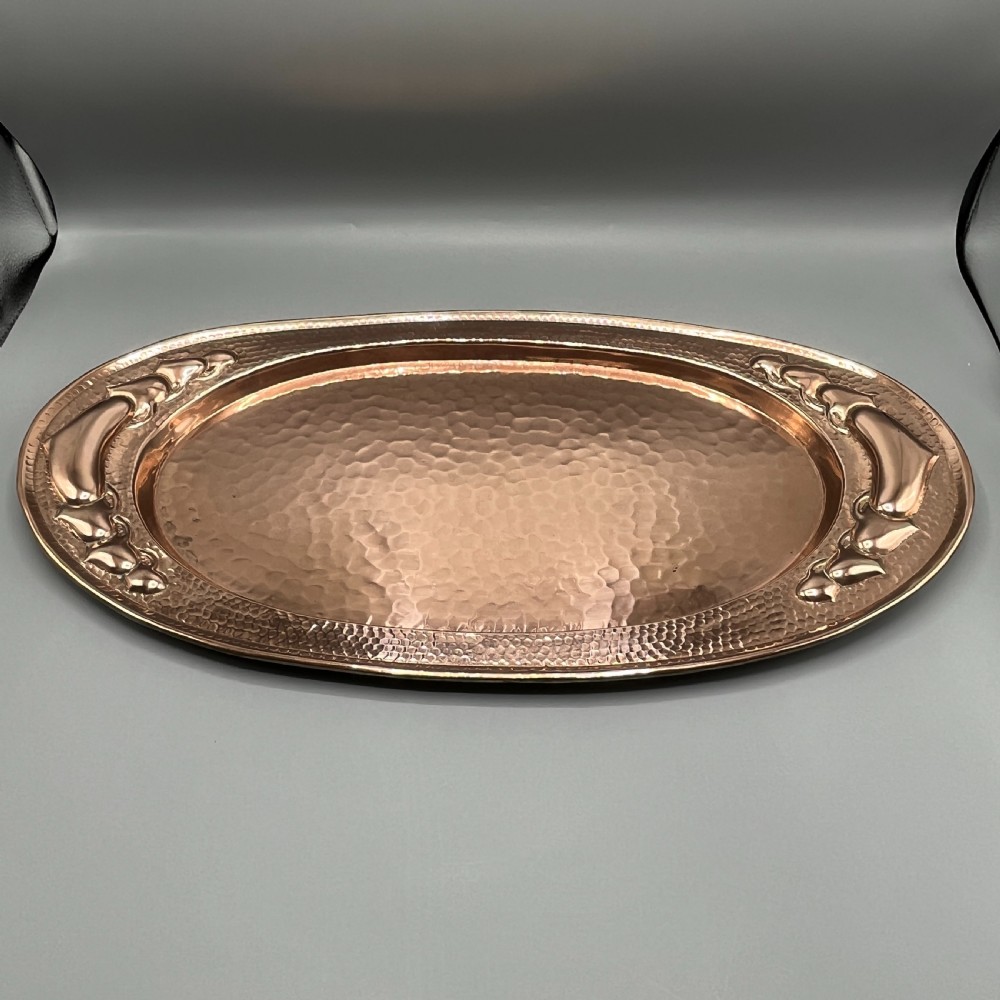 An oval Arts and Crafts copper tray featuring a planished hammered centre and stylised repousse detailing around the rim. View II