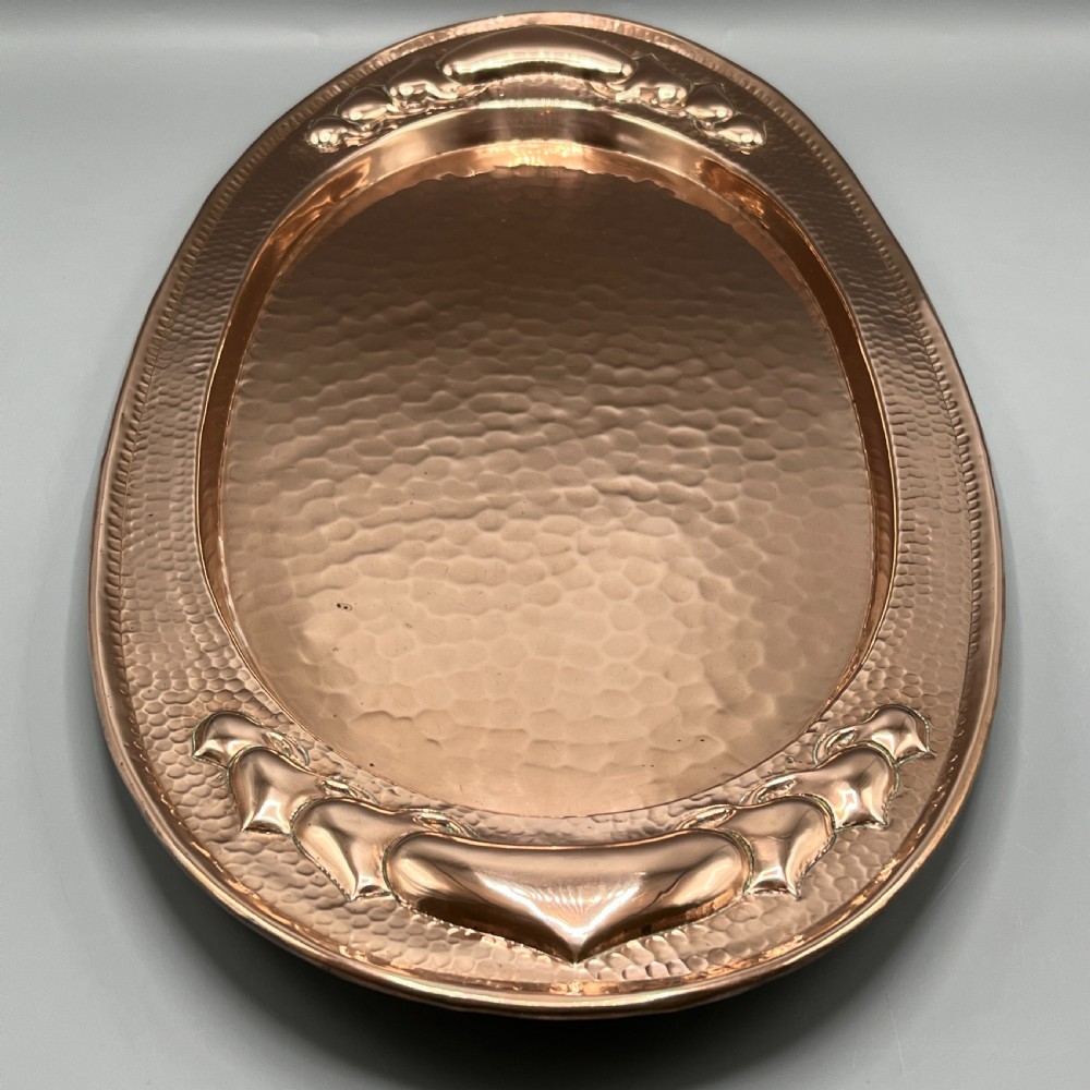 An oval Arts and Crafts copper tray featuring a planished hammered centre and stylised repousse detailing around the rim. View III