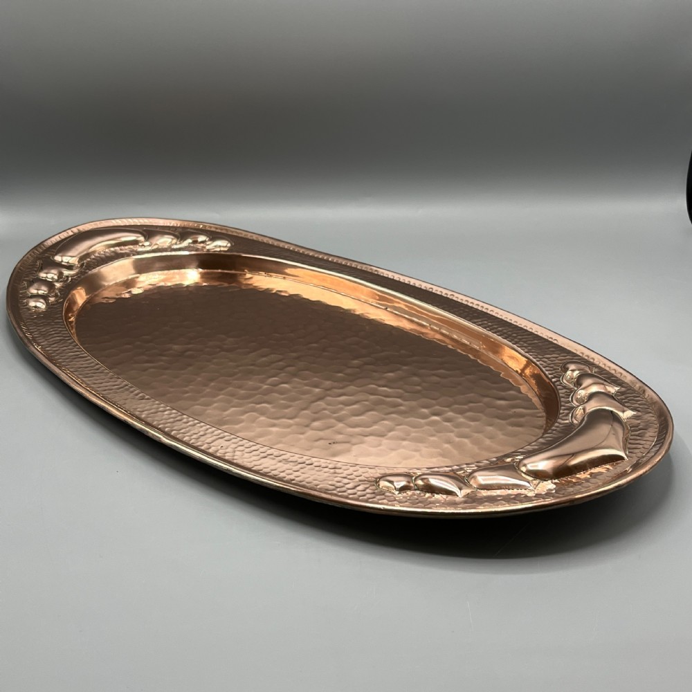 An oval Arts and Crafts copper tray featuring a planished hammered centre and stylised repousse detailing around the rim. View IV